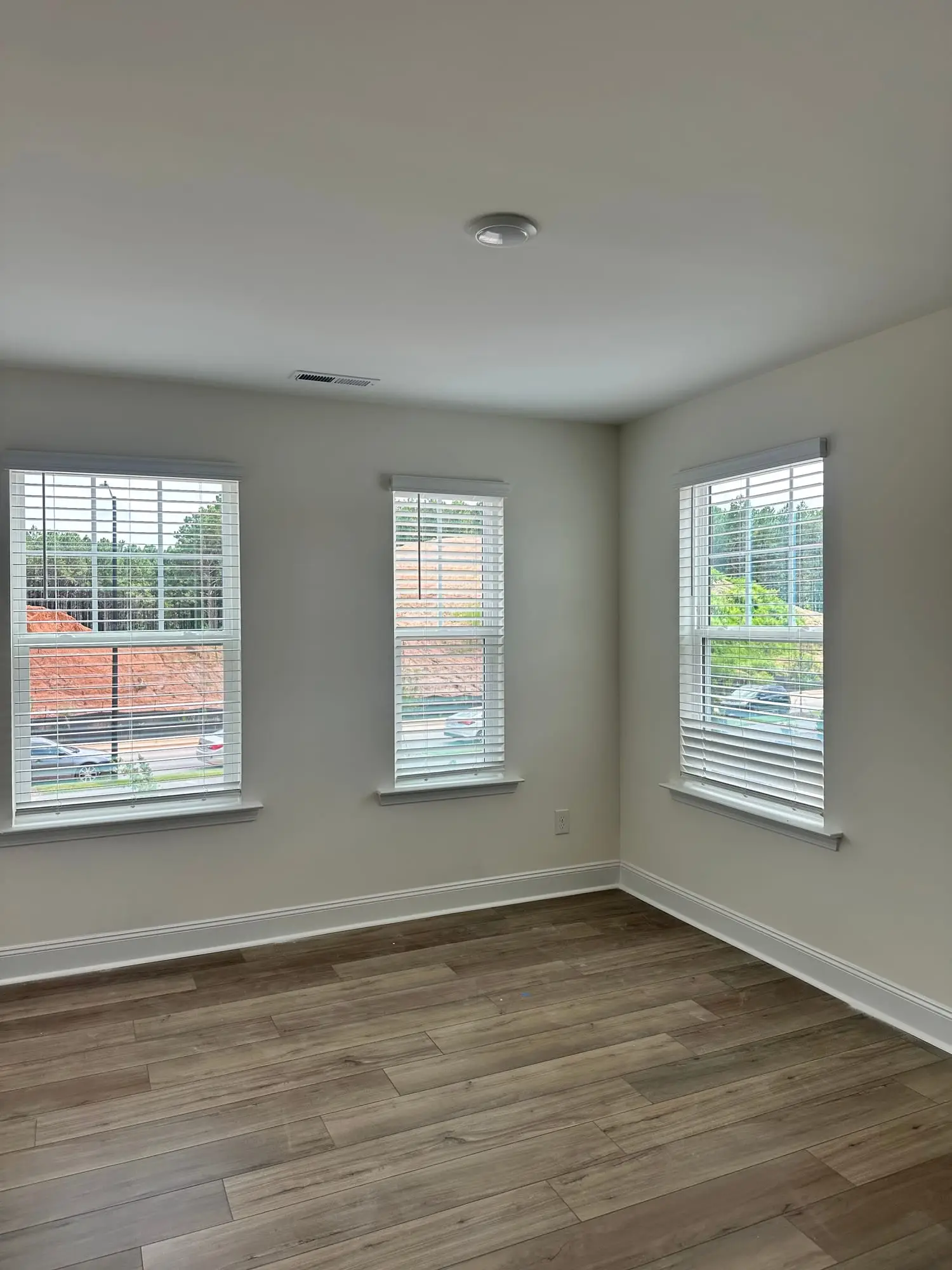 White faux-wood blinds installed on three windows of a newly finished room by JND Home Solutions