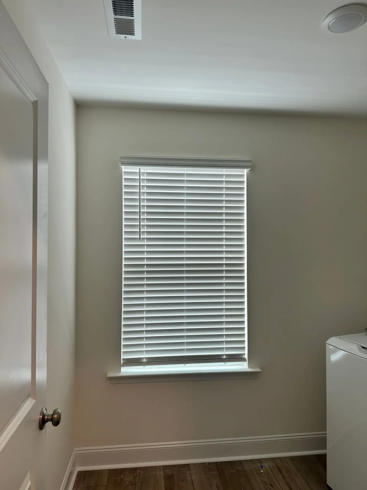 White faux-wood blinds hung on a laundry room window