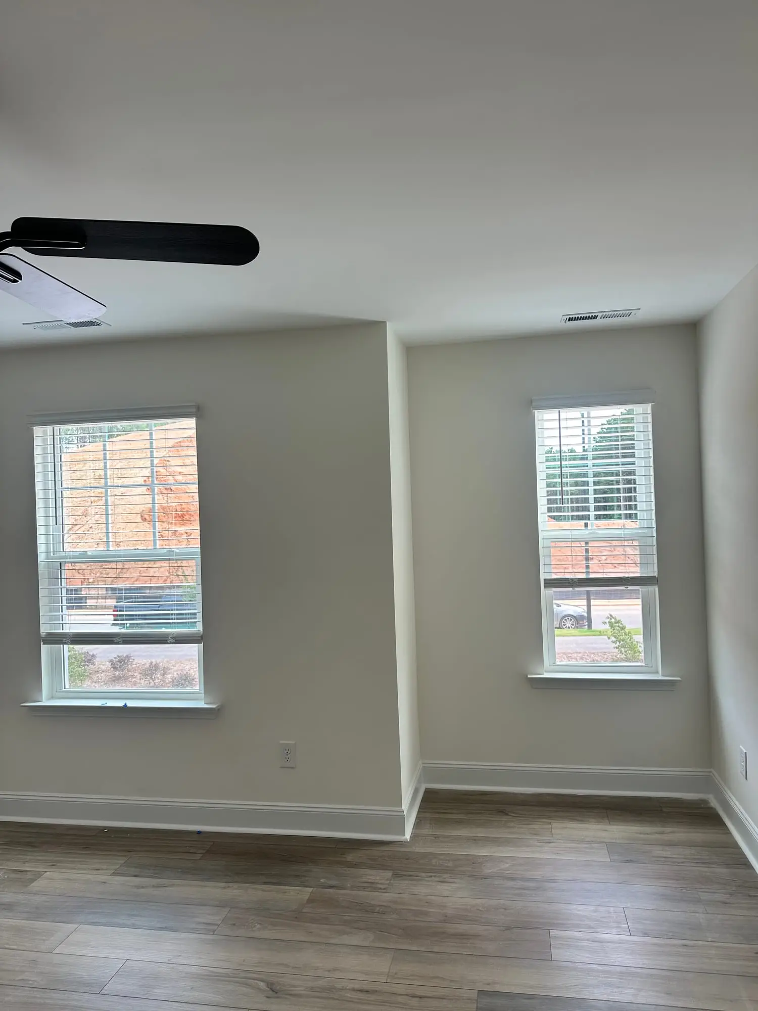 Two bedroom windows fitted with white blinds under a black ceiling fan