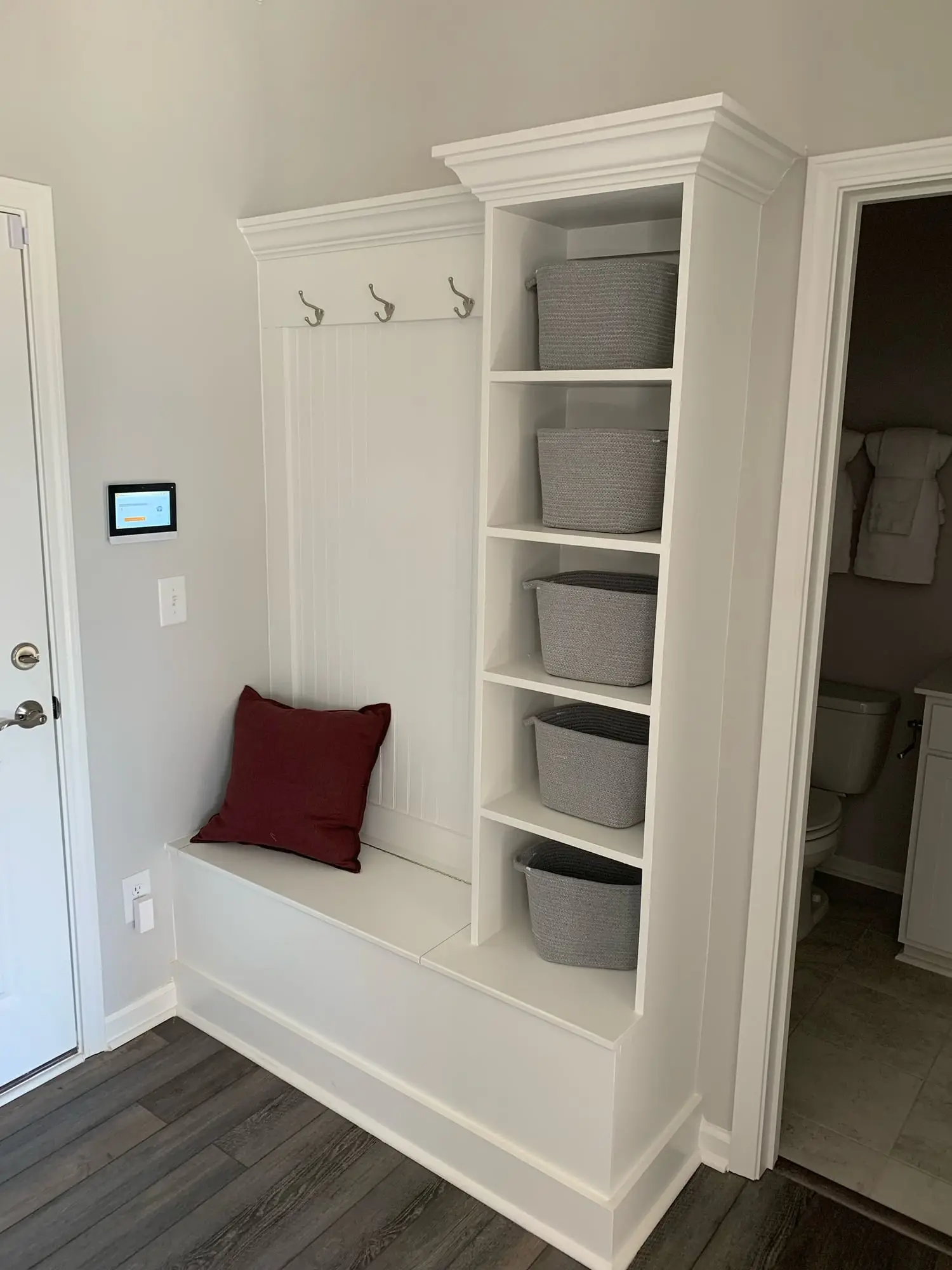 Custom white mudroom bench with coat hooks and a basket shelf tower built as a back-door drop zone by JND Home Solutions